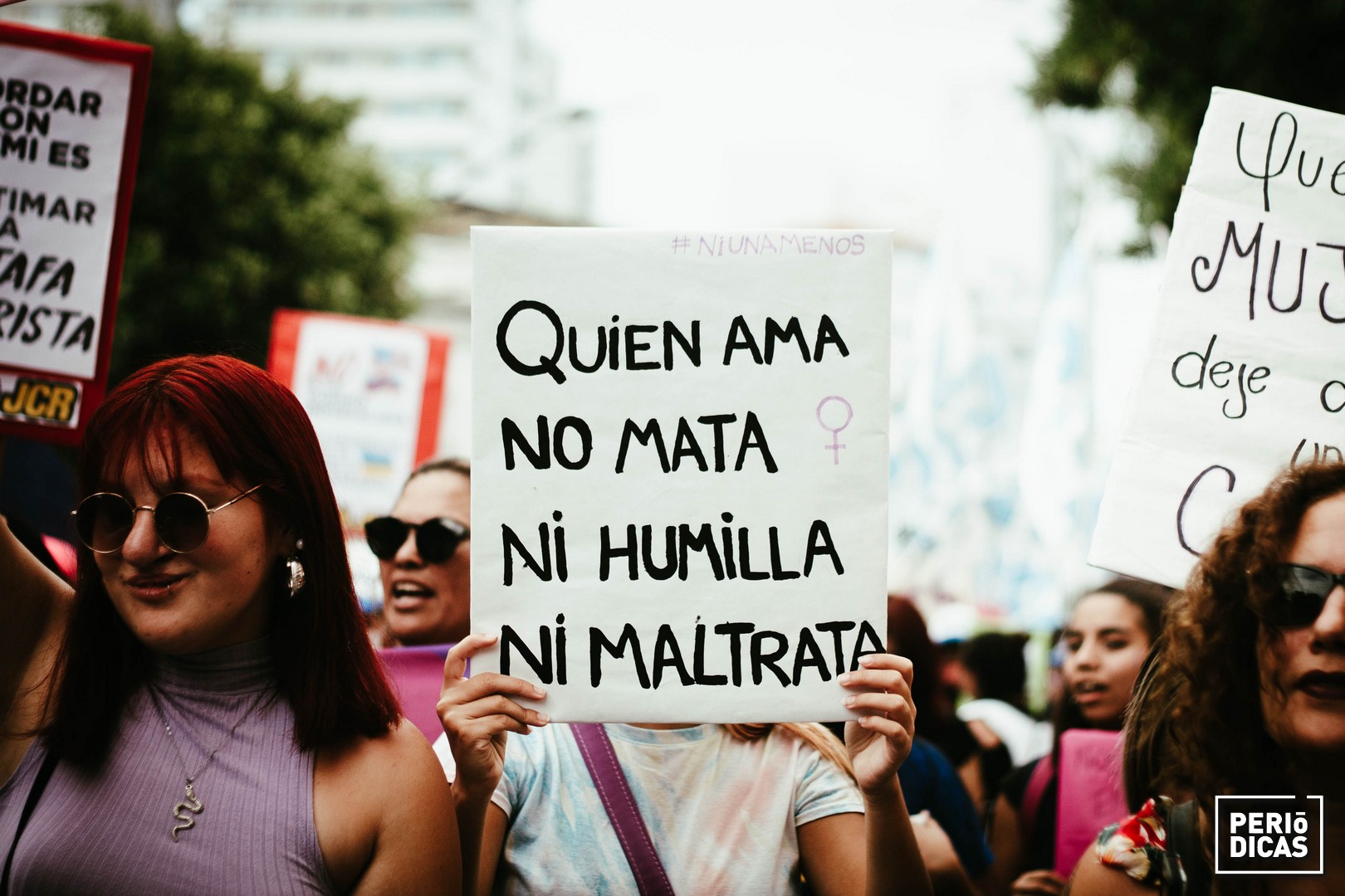 Joven sostiene cartel blanco con letras negras que dice "quien ama no mata ni humilla ni maltrata" en la marcha del 8 de marzo de 2022