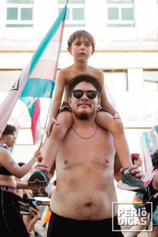Varon trans con gafas negras lleva a un niño trans montado en su cuello durante la Marcha del Orgullo 2022 de Santa Fe
